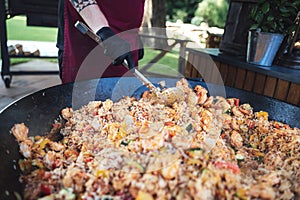 Man preparing meal in huge pan. One-pan food probably Paella. Male hand stirring ingredients. Celebration, party