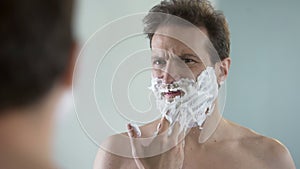 Man preparing to shave, feeling discomfort and tingle on face from shaving foam