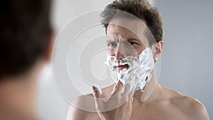 Man preparing to shave, feeling discomfort and tingle on face from shaving foam