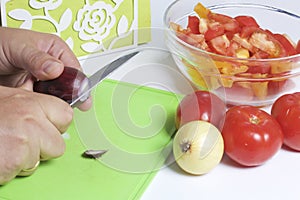 A man is preparing a vegetable salad. He cuts the onion on a cutting board.