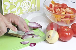 A man is preparing a vegetable salad. He cuts the onion on a cutting board.