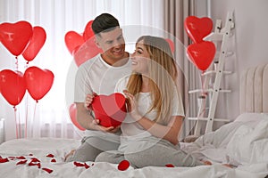 Man presenting gift to his girlfriend in room decorated with heart shaped balloons. Valentine`s day celebration