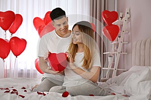 Man presenting gift to his girlfriend in room decorated with heart shaped balloons. Valentine`s day celebration