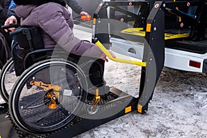 A man presses a button on the control panel to pick up a woman in a wheelchair in a taxi for the disabled. Black lift specialized