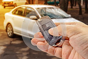 Man presses button on ignition key with immobilizer on the background of the car