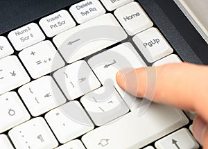 Man pressing the enter key on a simple plain white laptop keyboard, finger closeup, detail, hand up close. Decision confirmation