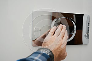 A man is pressing a wall-mounted polished chrome single flush plate to flush the toilet