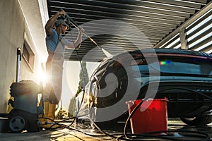 Man Pressure Washing His Modern Car Inside a Carport photo