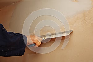 Man is priming a surface with a palett knife.  Maintenance repair works renovation in the flat. Restoration indoors. Concrete