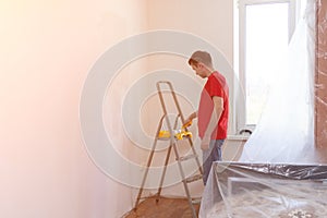 Man priming the wall with a roller. Repair of the interior. Young male decorator painting a wall in house. Concept