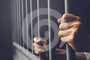 Man in prison hands of behind hold Steel cage jail bars.