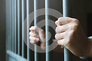 Man in prison hands of behind hold Steel cage jail bars.