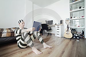 Man in Prisoner Uniform at Home Sitting on Floor and Reading a Book. Lockdown Concept