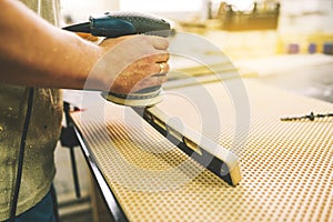 A man processes a wooden part with a grinder. Manufacturing of furniture in a carpentry workshop. Wood polishing machine