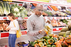 Man in produce section of supermarket choosing sweet paper and bananas