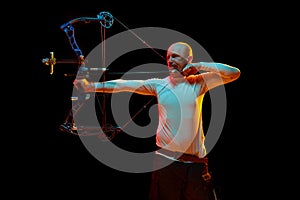 Man, professional archer training, aiming archery bow into target against black studio background in neon light. Archery