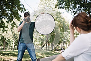 Man with professional camera and reflector shooting in park