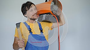 A man professional home renovator holds a Propane Hot Air Heater and a hook for stretch ceiling installation in his arms