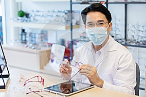 Man professional optician selling wear protective face mask sitting checking details quality of eyeglasses.