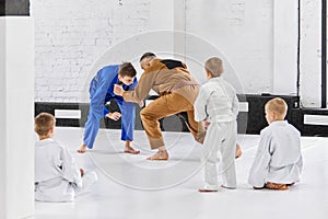 Man, professional sport coach teaching boys, children judo, jiu-jitsu fight activity. Professional athletes and kids.