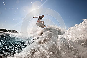 Man professionally rides and bounces on surf style wakeboard over splashing wave against blue sky photo