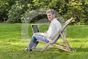 Man on profile sitting with laptop computer on garden chair