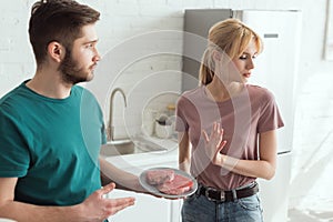 man proposing raw steaks to disgusted girlfriend