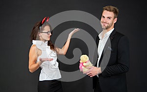 Man proposing with Valentines bear to angry girl in red devil horns dark background, Halloween