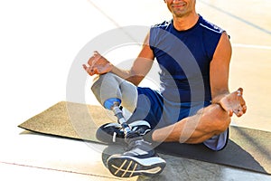 man with prosthesis leg practicing yoga sitting in lotus pose on yoga mat meditating outdoors in sun lights