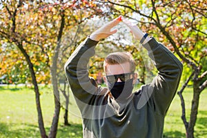 Man in a protective black mask making home sign in a city park. Copy space. Concept symbol home made by hands on the