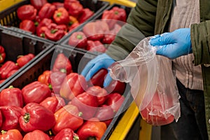 A man in protective blue gloves puts vegetables in a bag. Close-up, no face visible. Buying food during a pandemic