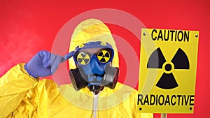 Man in Protective Chemical Suit, Protective Mask with a Poster. Caution Radiation Turns A Finger At The Temple. Studio