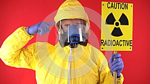 A man in a protective chemical suit, in a protective mask with the poster "Caution radiation" and twists his finger at