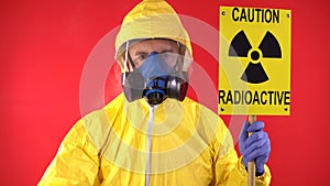 A man in a protective chemical suit, a protective mask shows a finger on the poster "Caution radiation". The concept of