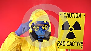A man in a protective chemical suit, protective mask shows his finger on the poster Caution radiation. Studio video