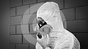 Man in protective clothing and a gas mask on an urban gray background - Worker during disinfection and decontamination for people