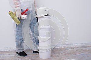A man in protective clothing, with paint rollers in his hands, put four buckets on top of each other, against the background of a