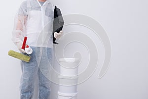 A man in protective clothing, with paint rollers in his hands, put three buckets on top of each other, against the background of a