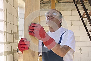 Man in protective gloves and glasses holding wooden beam.Working process during construction of house