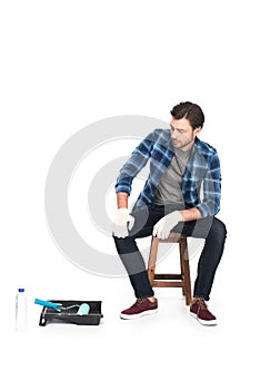 man in protective gloves resting on chair near roller tray and paint roller