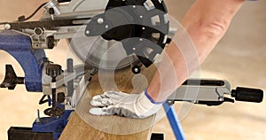 Man in protective gloves works with miter saw, cutting wooden board of laminate