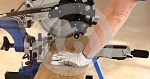 Man in protective gloves works with miter saw, cutting wooden board of laminate