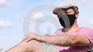 A man in a protective mask and cap sits in a camping chair. Outdoor recreation in self-isolation during a pandemic