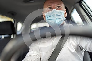 A man in a protective mask driving a car, steering wheel in the foreground