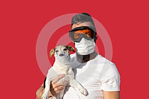 Man in protective mask and glasses holds cute jack russell dog in medical mask