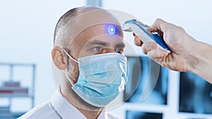 man in a protective mask is measuring the temperature with a digital thermometer.