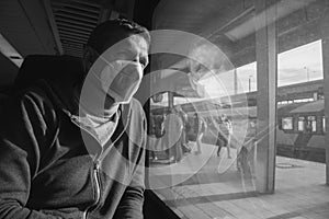 Man in protective mask N95 in train, black and white. Tourist looking in window inside of railway wagon, monochrome.