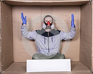 Man in a protective mask sits at a cardboard box, showing his helplessness