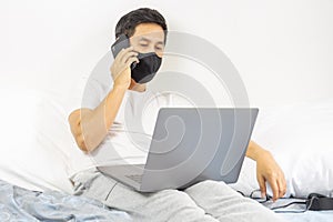 Man with protective mask talking on cell phone with laptop on laps working from home concept.