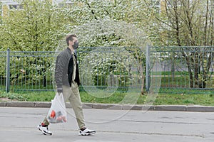 A man in a protective mask walks down the street with a bag of groceries